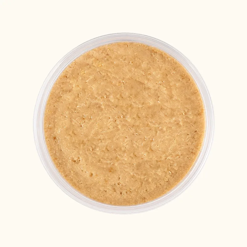 Orange-beige wet cat food with a finely textured surface in a round plastic cup